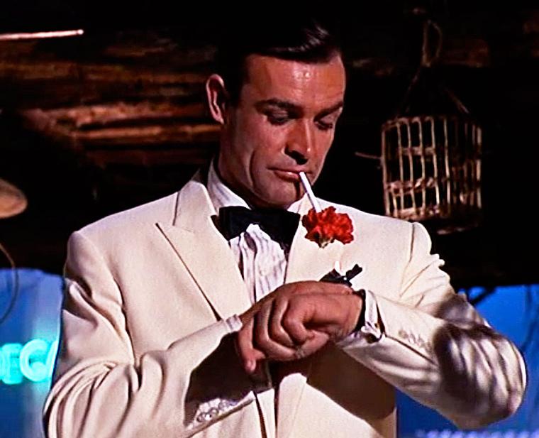 Sean Connery as 007 checking the time on his Rolex Submariner watch with a striped nylon strap during Goldfinger, the third Bond film.